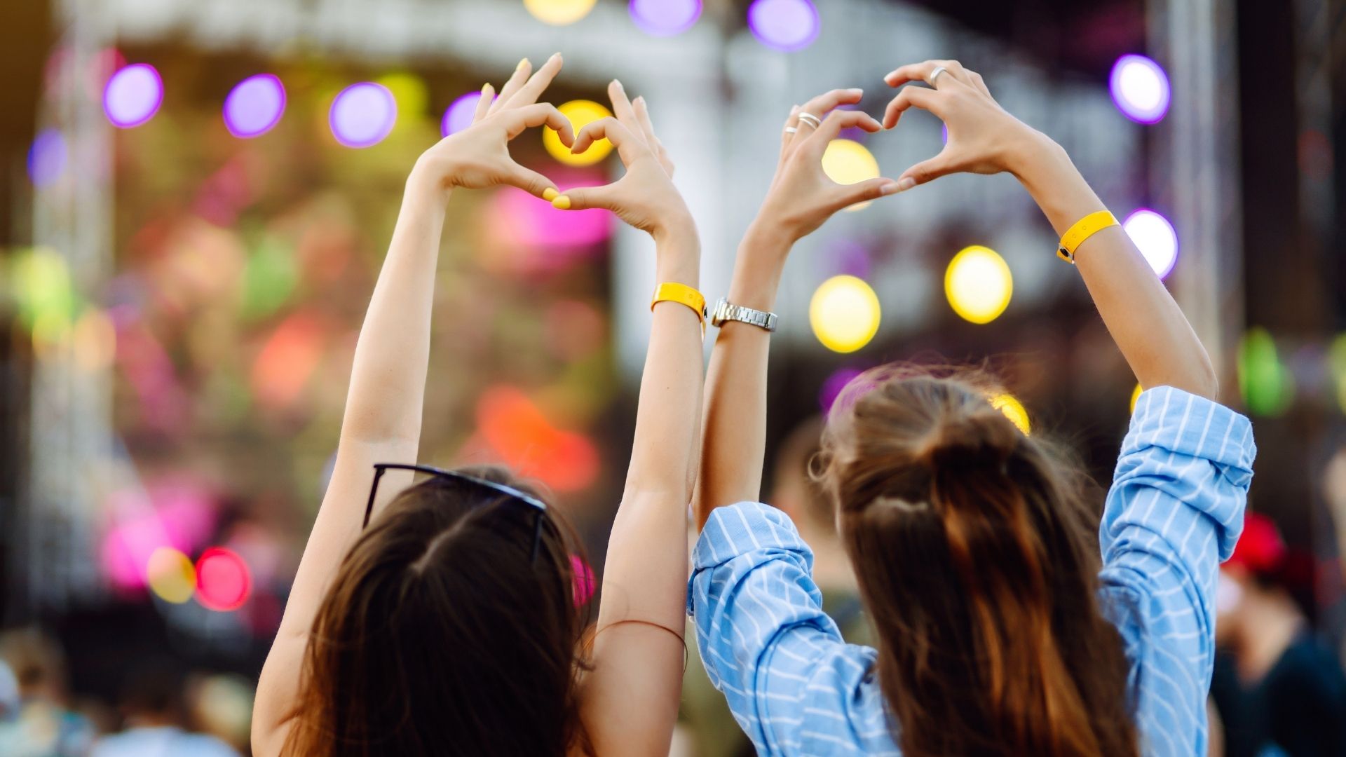 Back view of two ladies with their arms up making the heart shape sign